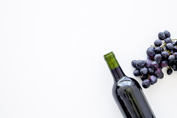 Red wine concept. Glass bottle with beverage near bunch of grapes on white background top view copy space