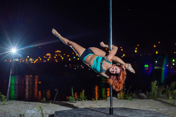 The red-haired woman spins on a pole against the background of the night city. A young woman dances...