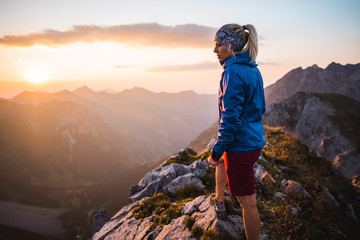 A Young Adventurous Sportive Girl enjoying a Beautiful Sunset on Top of a Peak in the Austrian Alps