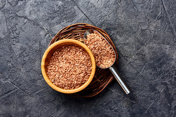 Wild brown rice in wooden bowl on black background. Top view of grains.