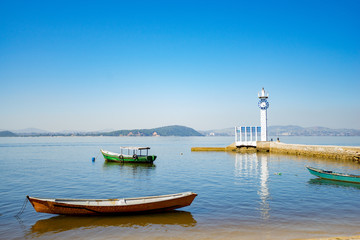 Fototapeta na wymiar Boats and pier with small lighthouse on the tropical island of Paqueta in the Guanabara bay in Rio de Janeiro with blue water and blue sky