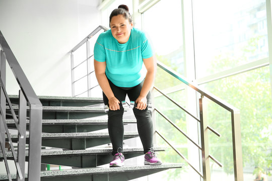 Tired Overweight Woman With Dumbbells On Stairs Indoors