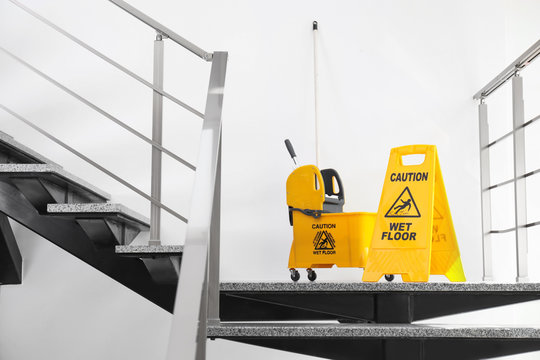 Safety sign with phrase Caution wet floor and mop bucket on stairs