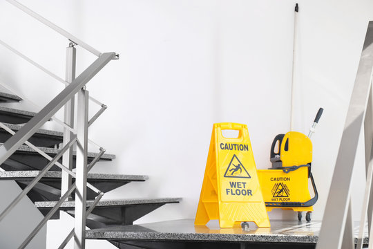 Safety sign with phrase Caution wet floor and mop bucket on stairs