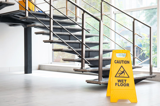 Safety sign with phrase Caution wet floor near stairs