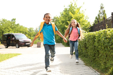 Cute little children with backpacks running outdoors. Elementary school