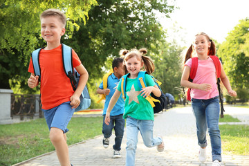 Cute little children with backpacks running outdoors. Elementary school