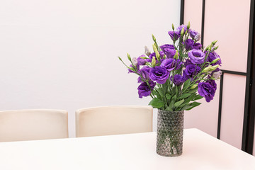 Vase with beautiful flowers on white table against color background. Stylish interior