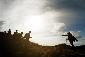 Silhouettes of hiking team with backpacks standing on top of wild grass mountain. Cloud and sunrise sky background. Color effect