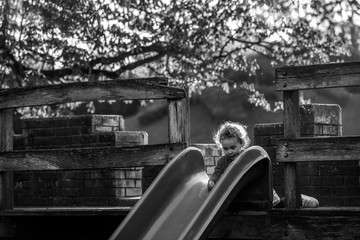 Naklejka na ściany i meble Girl on slide on playground. Active Child playing on outdoors playground in nature, happy girl smiling, healthy lifestyle, beautiful blond girl having fun on slide