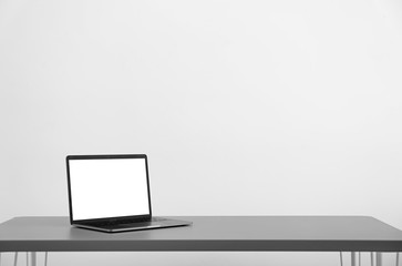 Modern laptop with blank screen on table against light background