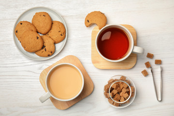 Flat lay composition with black tea, milk and cookies on wooden table