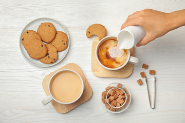 Woman pouring milk into cup with black tea on wooden table, top view