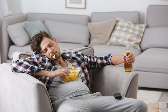 Lazy man with bottle of beer and chips sleeping in armchair at home