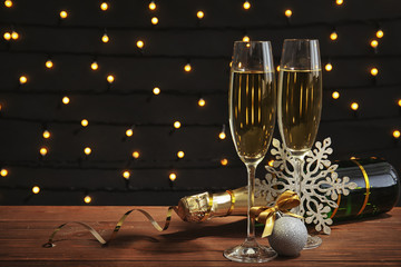 Glasses of champagne with bottle and festive decor on table against blurred fairy lights