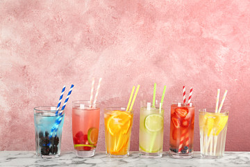 Glasses with lemonades on table against color background
