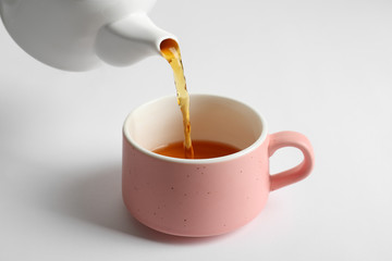 Pouring hot tea into ceramic cup on white background