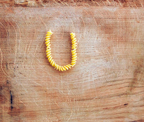 U letter done with pasta fusilli on a wooden chopping board