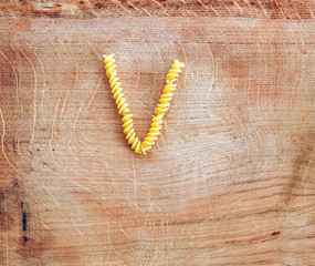 V letter done with pasta fusilli on a wooden chopping board