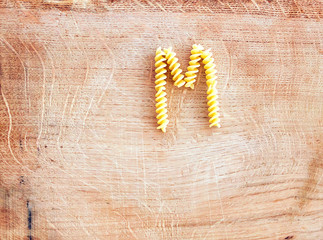 M letter done with pasta fusilli on a wooden chopping board