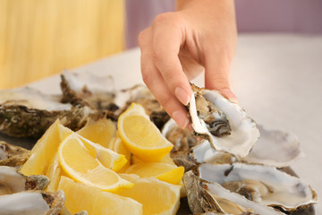 Woman holding fresh oyster over plate, focus on hand