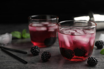 Glasses with iced blackberry lemonade on grey table against dark background