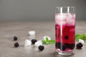 Glass with iced blackberry lemonade on grey table