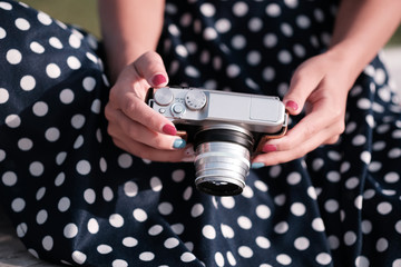 Oldschool mirrorless camera in the hands of a girl in a white and black dot dress