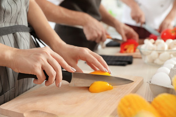 Female chef cutting paprika on wooden board at table, closeup