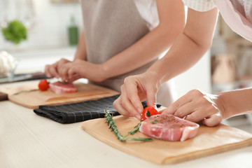 Female chef preparing meat on wooden board at table, closeup