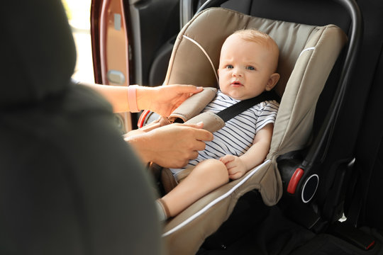 Mother fastening baby to child safety seat inside of car