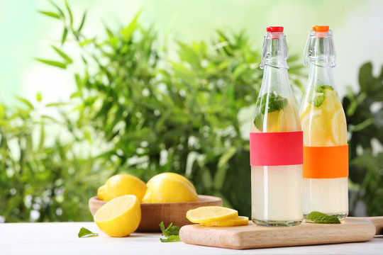 Bottles with natural lemonade on table against blurred background