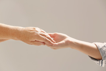 Helping hands on gray background, closeup. Elderly care concept