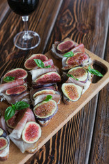 Healthy bruschettas with bread, cream cheese, prosciutto, figs and basil on rustic wooden table