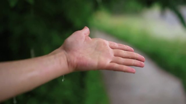 Hand of a young unrecognizable woman with long fingernails under the rain touching the water. Summer. Concept of being calm and enjoying the weather. Loving nature. Handheld slow motion medium shot