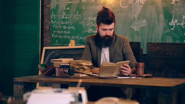 A bearded teacher summarizes and reads a book in a school classroom on a background of a green board. Learning concept. School children in uniform. Teacher in classroom.