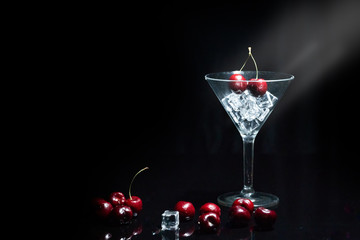 Close up view of cherry in a martini glass among ice in black background with flare.