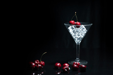 Close up view of cherry in a martini glass among ice in black background.