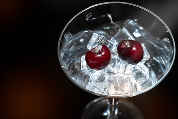 Close up view of cherry in a martini glass among ice in black background with flare and foreground.