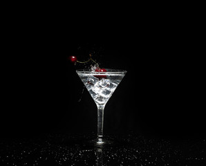 Close up view of splash water with falling cherry in a martini glass among ice in black background.