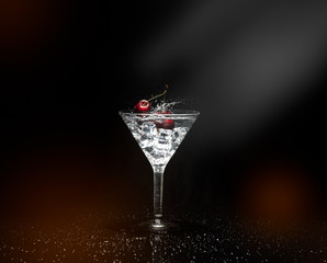 Close up view of splash water with falling cherry in a martini glass among ice in black background with flare and foreground.