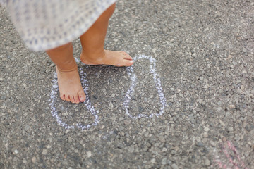 Kind malt Fußabdruck mit Kreide auf Boden. Child draw footprint with street crayon.
