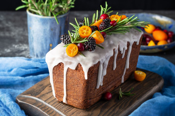 Loaf cake with icing glaze decorated fresh berries and rosemary on wooden chopping board.