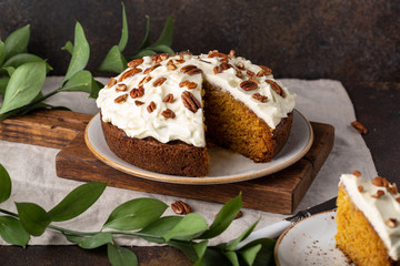 Carrot cake with whipped frosting and pecans on dark background.