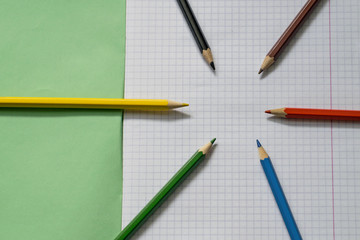 Blank paper and colorful pencils. Colored pencils on a notebook sheet. School notebook. View from above.