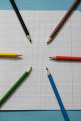 Blank paper and colorful pencils. Colored pencils on a notebook sheet. School notebook. View from above.