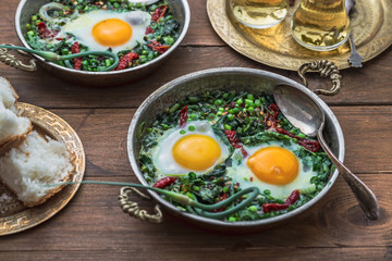 Green shakshuka. Fried eggs with fresh spinach, ramson, leek in a pan on a gray background, top view