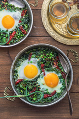 Green shakshuka. Fried eggs with fresh spinach, ramson, leek in a pan on a gray background, top view