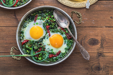 Green shakshuka. Fried eggs with fresh spinach, ramson, leek in a pan on a gray background, top view
