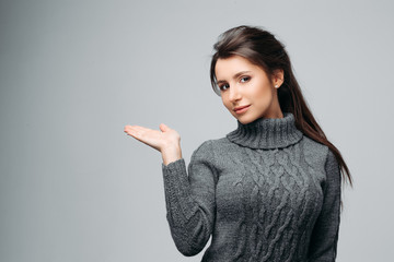 Waist up portrait of beautiful girl showing empty copy space in left side. Pretty brunette with stylish hairdo and perfect makeup. Isolated on gray background © Вячеслав Косько